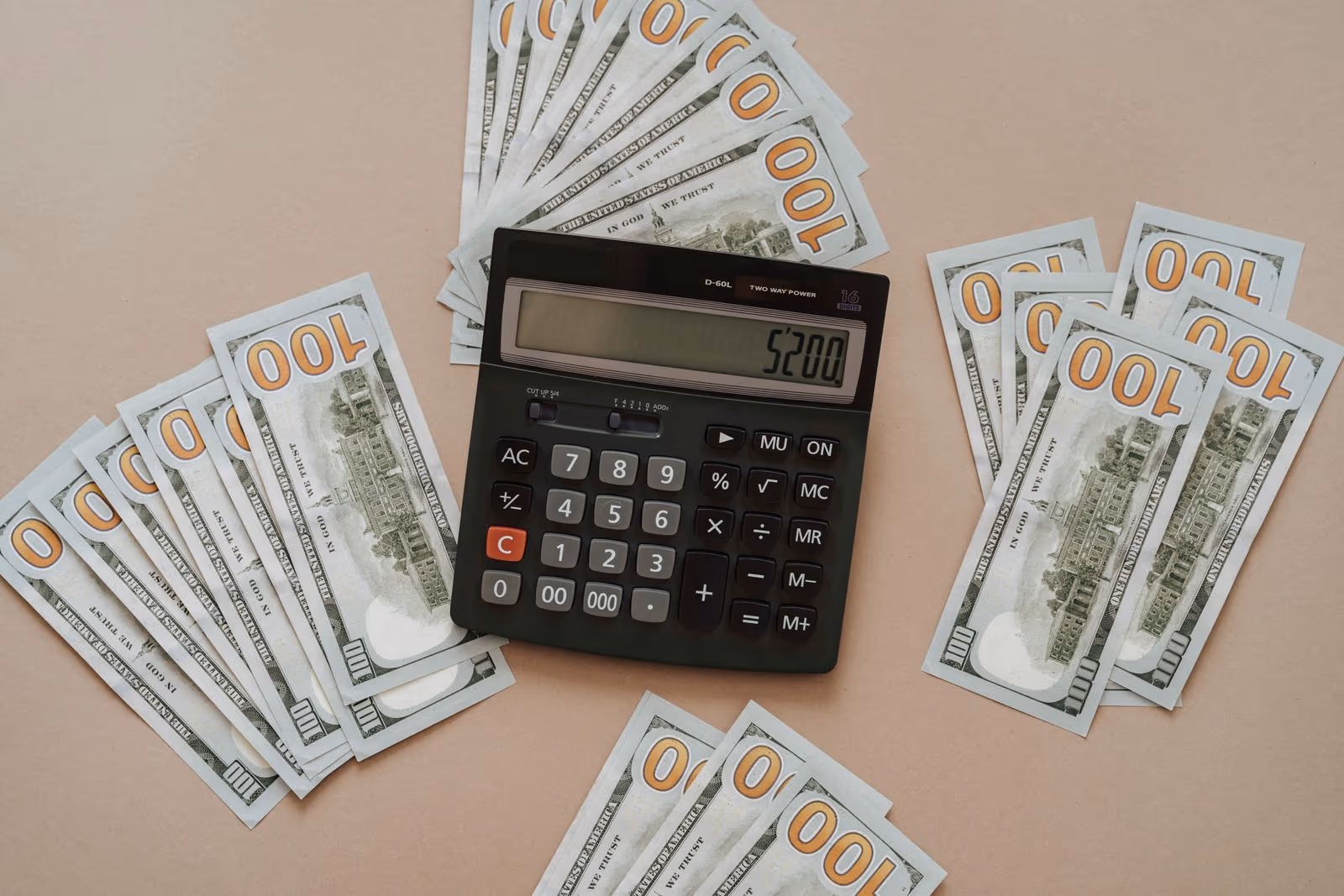 A calculator resting on a fan of U.S. hundred-dollar bills — the true cost of a discount Cook Islands Trust
